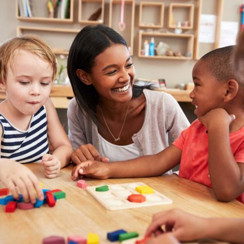 Teacher And Pupils Using Wooden Shapes In Montessori School