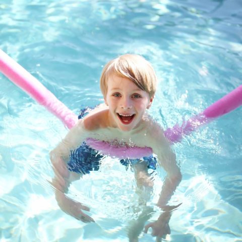 Happy Young Child Floating In Swimming Pool